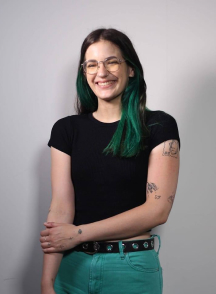 Young woman smiles at the camera. She is wearing green pants and a black top.