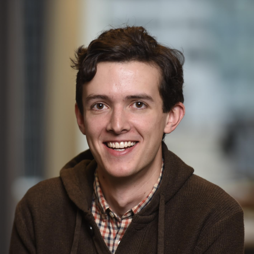 Headshot of Jon Campbell, a man with short dark hair. He is wearing a plaid shirt and a brown jacket.