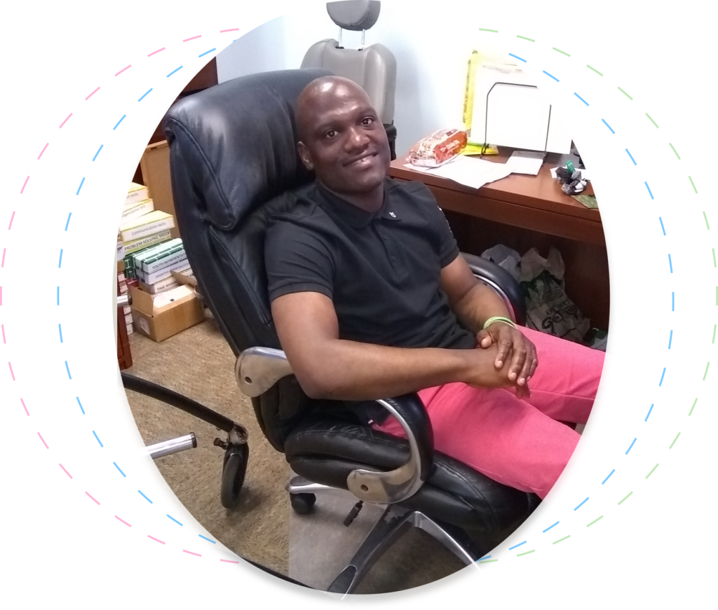 Aerius Franklin sitting in an office chair wearing a black collared shirt and red pants.